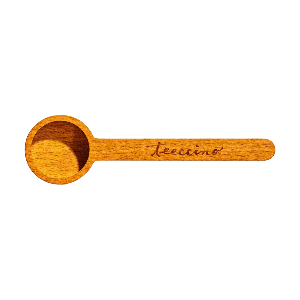 wooden measuring scoop with a smooth, natural finish is shown on a transparent background. The scoop features a round bowl and a long handle engraved with the Teeccino logo. Designed for portioning herbal coffee or tea, this lightweight wooden scoop adds a warm, rustic touch to the brewing routine while providing a practical, reusable measuring tool.