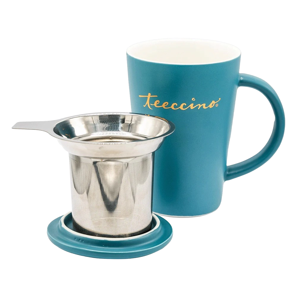 A teal Teeccino ceramic mug with gold logo stands beside a stainless steel reusable tea infuser and matching lid. The infuser features a fine mesh basket and wide rim for easy brewing. This coordinated set is designed for brewing herbal coffee or tea, offering a simple, reusable, and stylish way to enjoy caffeine-free Teeccino beverages at home