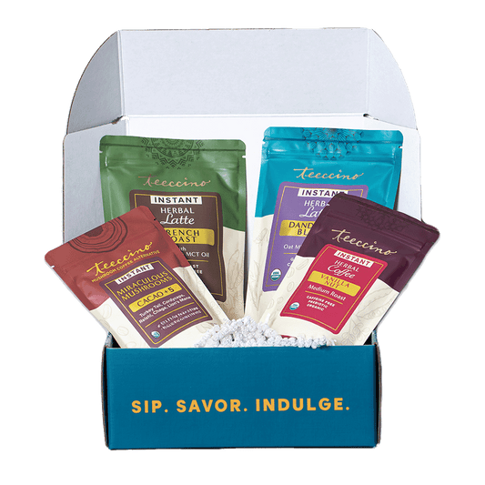 Teeccino assorted instant herbal latte sampler gift box opened to show multiple flavored packets inside, including mushroom, dandelion, and herbal coffee alternatives, arranged in a branded box with the phrase “Sip. Savor. Indulge.”