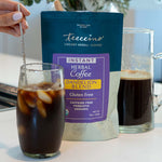 Bag of Instant Dandelion blend herbal coffee, a pitcher and a glass with black liquid and a hand from the left stirring the glass with a spoon